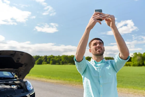 Hombre con teléfono inteligente y coche roto en el campo — Foto de Stock