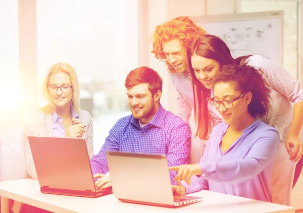 Equipe sorridente com computadores portáteis no escritório — Fotografia de Stock