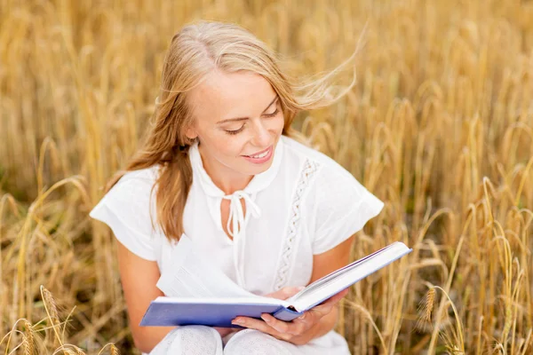 Giovane donna sorridente che legge il libro sul campo dei cereali — Foto Stock