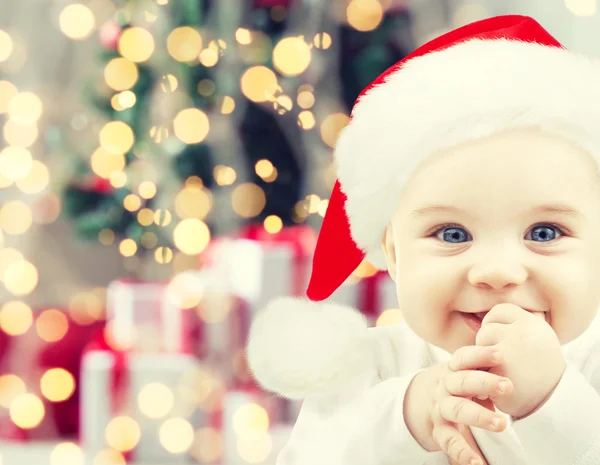 Happy baby in santa hat over christmas lights — Stock Photo, Image