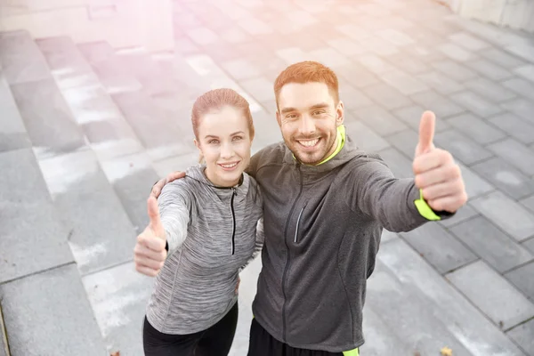 Sonriente pareja mostrando pulgares en la calle de la ciudad — Foto de Stock