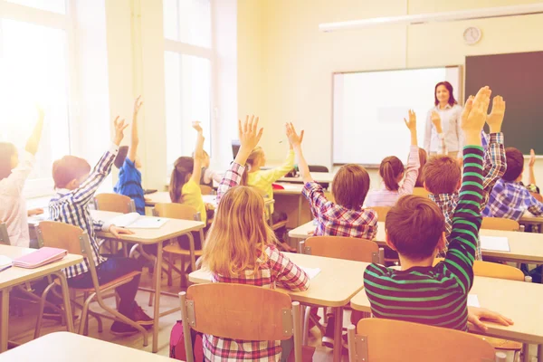 Grupo de crianças da escola levantando as mãos em sala de aula — Fotografia de Stock