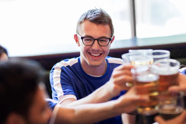 Football fans clinking beer glasses at sport bar — Stock Photo, Image