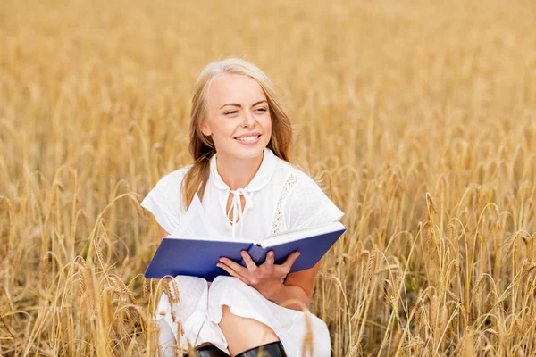 Giovane donna sorridente che legge il libro sul campo dei cereali — Foto Stock