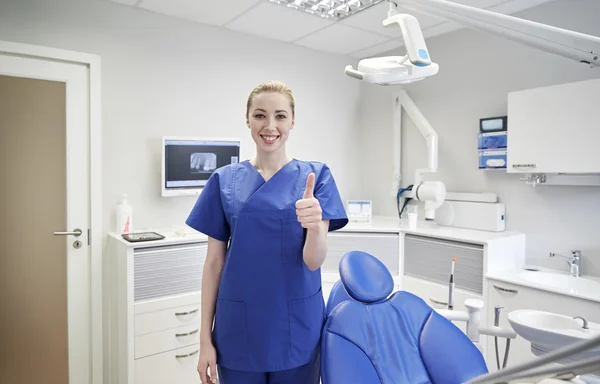 Dentista mujer feliz mostrando pulgares hacia arriba en la clínica — Foto de Stock