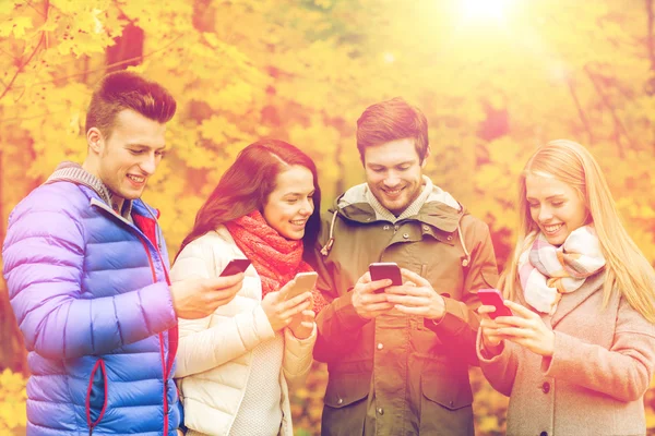 Amis souriants avec smartphones dans le parc de la ville — Photo