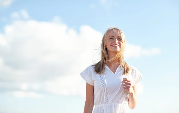 Beyaz elbiseli genç kadın üzerinde mavi gökyüzü gülümseyen — Stok fotoğraf