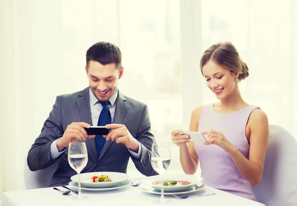 Smiling couple with appetizers and smartphones — Stock Photo, Image