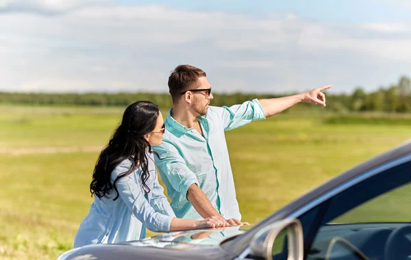 Man and woman with car pointing finger outdoors — Stock Photo, Image