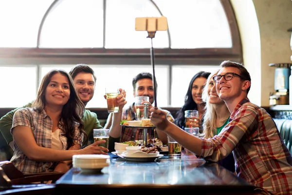 Gelukkige vrienden met selfie stok op bar of pub — Stockfoto