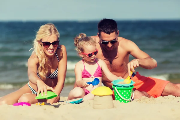 Família feliz brincando com brinquedos de areia na praia — Fotografia de Stock