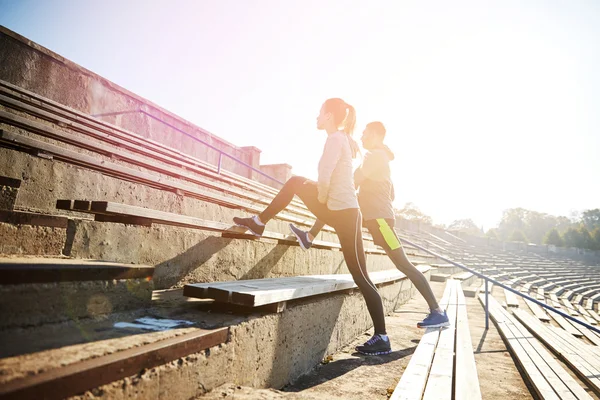 Couple stretching leg on stands of stadium — Stock Photo, Image