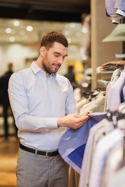 Gelukkig jonge man kiezen kleren in kledingwinkel — Stockfoto