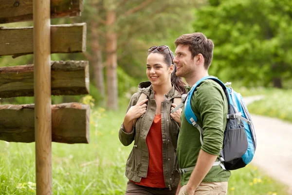 Couple souriant au panneau avec sacs à dos randonnée — Photo