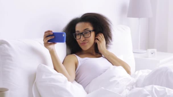 African woman with smartphone in bed at home — Stock Video