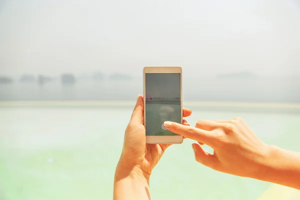 Primer plano de la mano femenina con smartphone en la playa — Foto de Stock