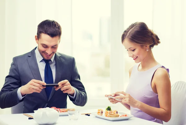 Casal sorridente com sushi e smartphones — Fotografia de Stock