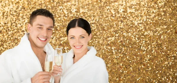 Happy couple in spa bath robes drinking champagne — Stock Photo, Image
