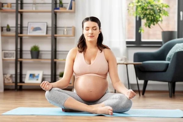 Pregnant woman with earphones meditating at home — Stock Photo, Image