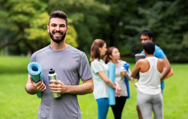 Uomo sorridente con stuoia di yoga sopra il gruppo della gente — Foto Stock