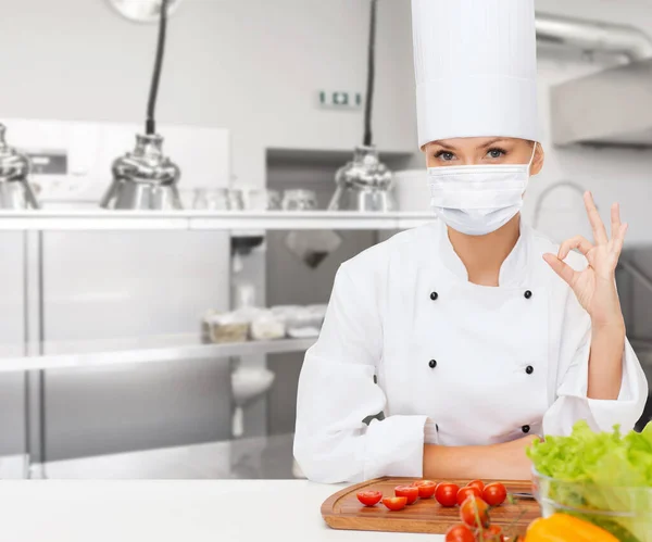 Mujer chef en máscara mostrando ok signo en la cocina —  Fotos de Stock