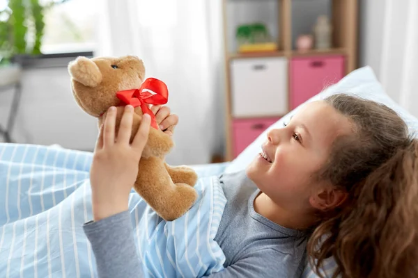 Niña feliz con oso de peluche acostado en la cama —  Fotos de Stock