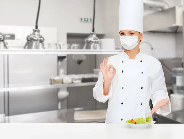 Mujer chef en máscara mostrando ok signo en la cocina — Foto de Stock