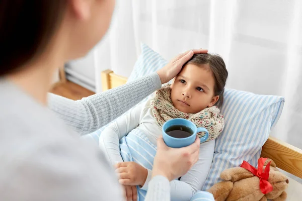 Mother giving tea to sick daughter lying in bed — Stock Photo, Image
