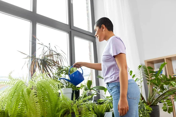 Afrikanska amerikanska kvinna vattna växter hemma — Stockfoto