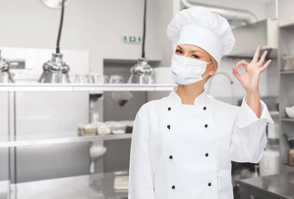 Chef feminino em máscara mostrando sinal ok na cozinha — Fotografia de Stock