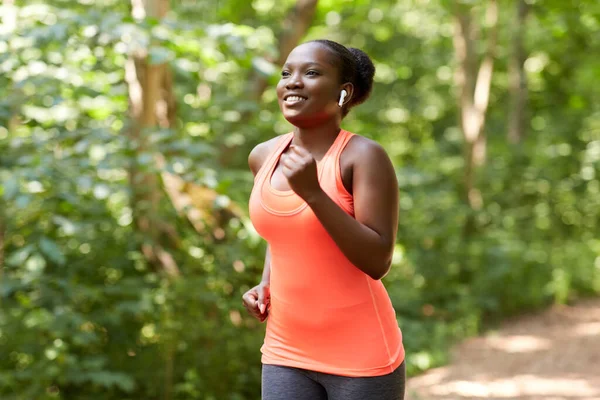 Femme africaine heureuse dans les écouteurs fonctionnant dans le parc — Photo