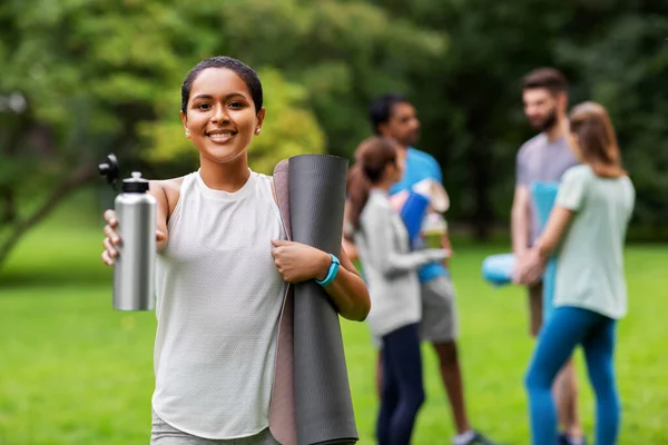 Donna sorridente con tappetino yoga e bottiglia al parco — Foto Stock