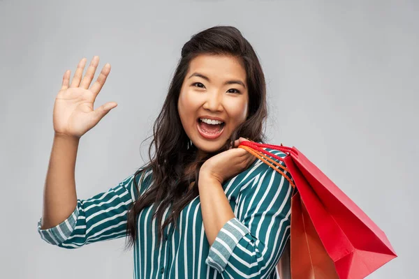 Feliz asiático mujer con compras bolsas ondeando mano — Foto de Stock