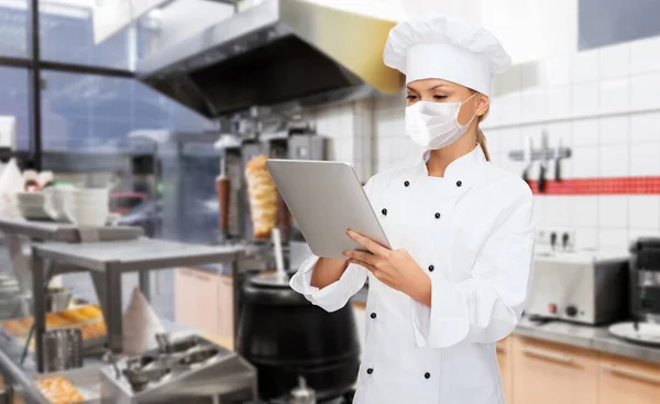 Vrouwelijke chef in masker met tablet pc in de keuken — Stockfoto