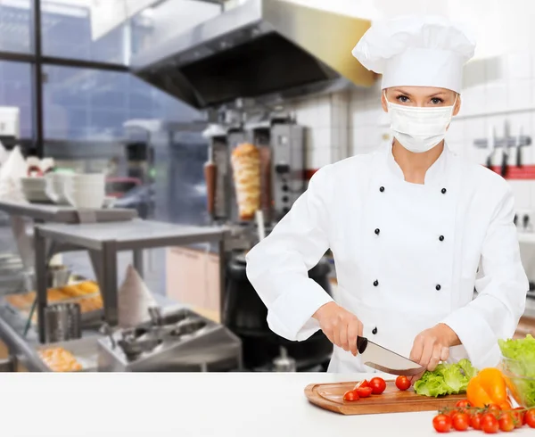 Female chef in mask cutting vegetables at kitchen — Stock Photo, Image