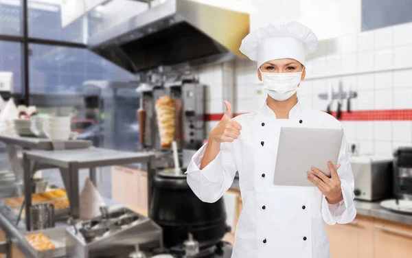 Chef feminino em máscara com tablet pc na cozinha — Fotografia de Stock