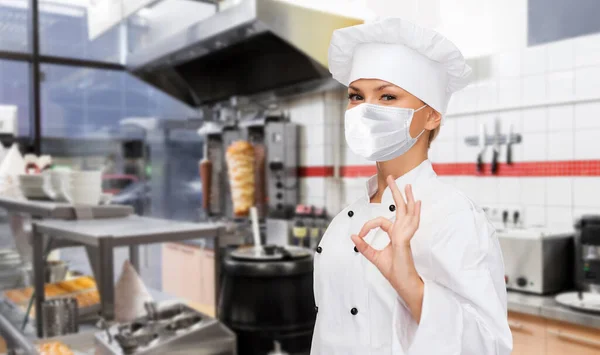 Chef donna in maschera mostrando segno ok in cucina — Foto Stock