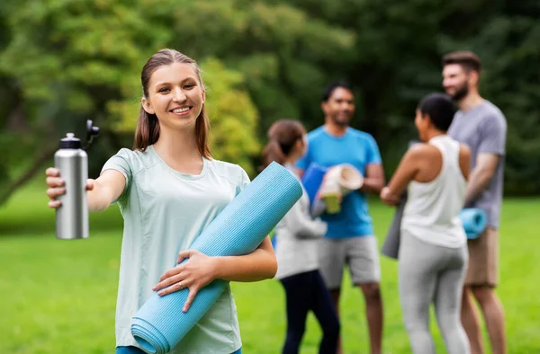 Mujer sonriente con esterilla de yoga y botella en el parque —  Fotos de Stock