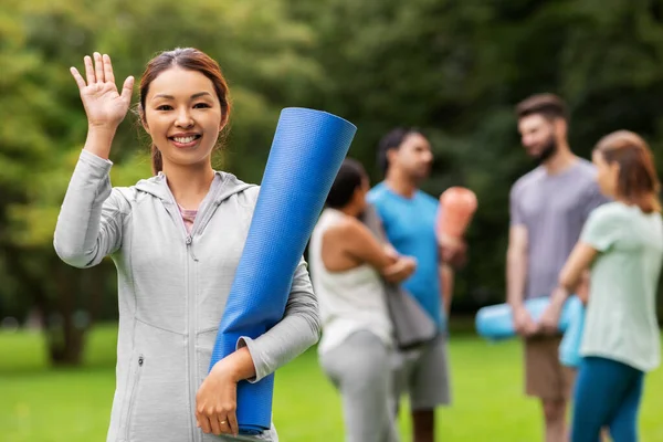 Donna sorridente con tappetino yoga mano agitante al parco — Foto Stock