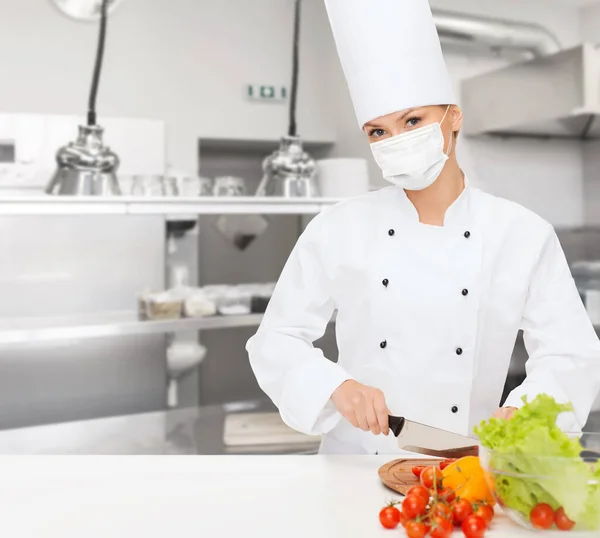 Female chef in mask cutting vegetables at kitchen — Stock Photo, Image