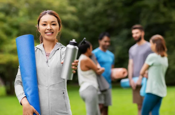 Femme souriante avec tapis de yoga et bouteille au parc — Photo