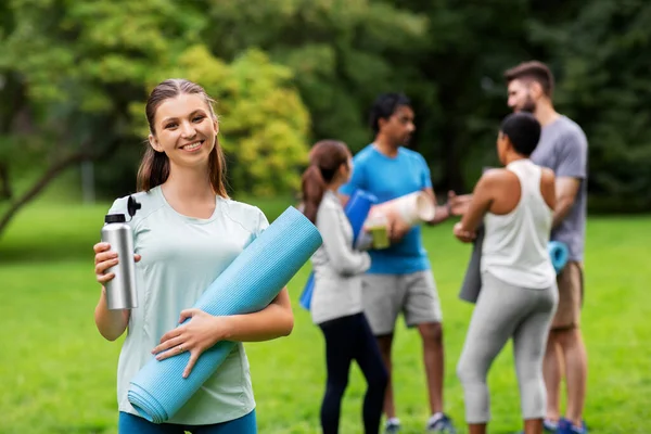 Mujer sonriente con esterilla de yoga y botella en el parque Fotos de stock libres de derechos