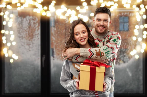 Feliz pareja en suéteres de Navidad con caja de regalo —  Fotos de Stock