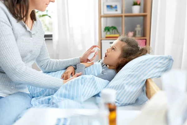 Mother with oral spray treats sick little daughter — Stock Photo, Image