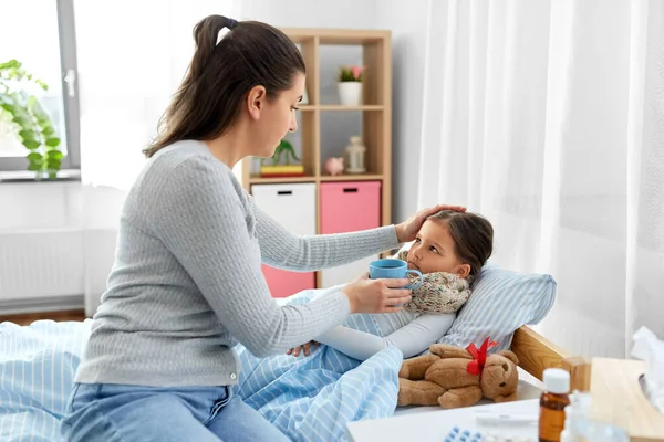 Moeder geeft thee aan zieke dochter liggend in bed — Stockfoto