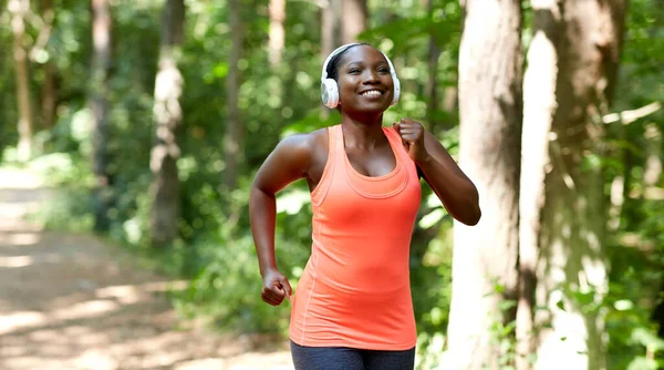 Mujer africana feliz en auriculares corriendo en el parque — Foto de Stock