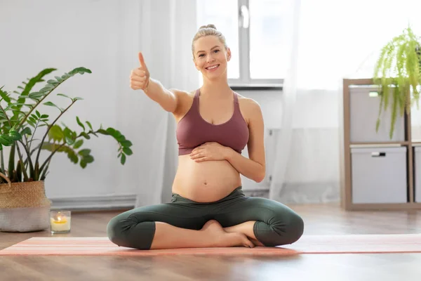 Pregnant woman shows thumbs up sitting on yoga mat — Stock Photo, Image