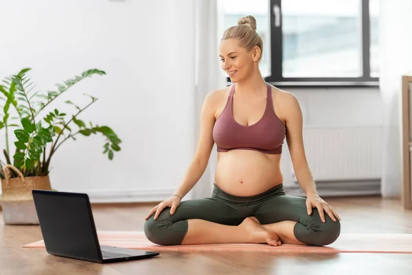 Pregnant woman with laptop doing yoga at home — Stock Photo, Image