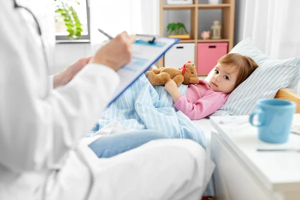 Médico com prancheta e menina doente na cama em casa — Fotografia de Stock