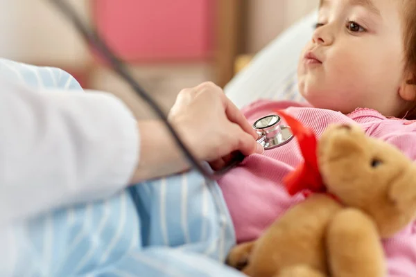 Läkare med stetoskop och sjuk flicka i sängen — Stockfoto